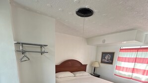 Une chambre à coucher avec un lit, une table de chevet, une lampe, un tableau au mur et une fenêtre avec des rideaux.