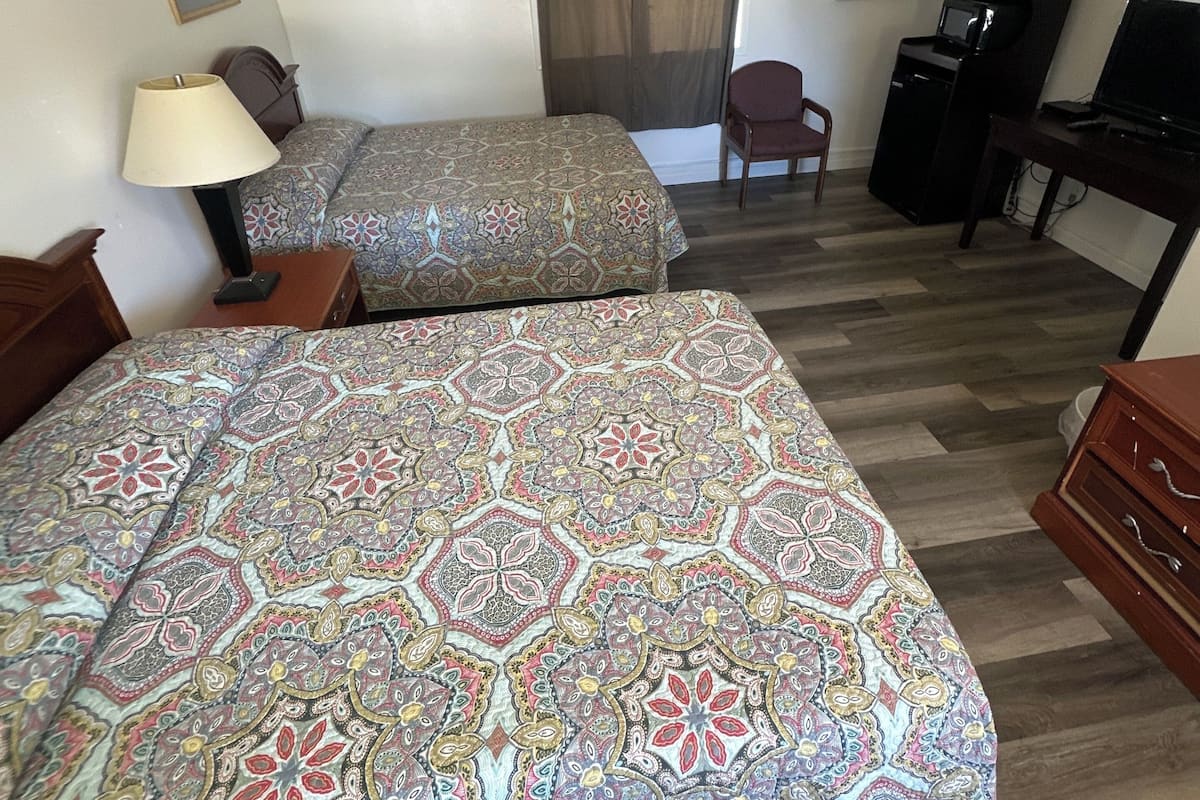 A hotel room with two beds, a desk, a chair, a TV, and a lamp.