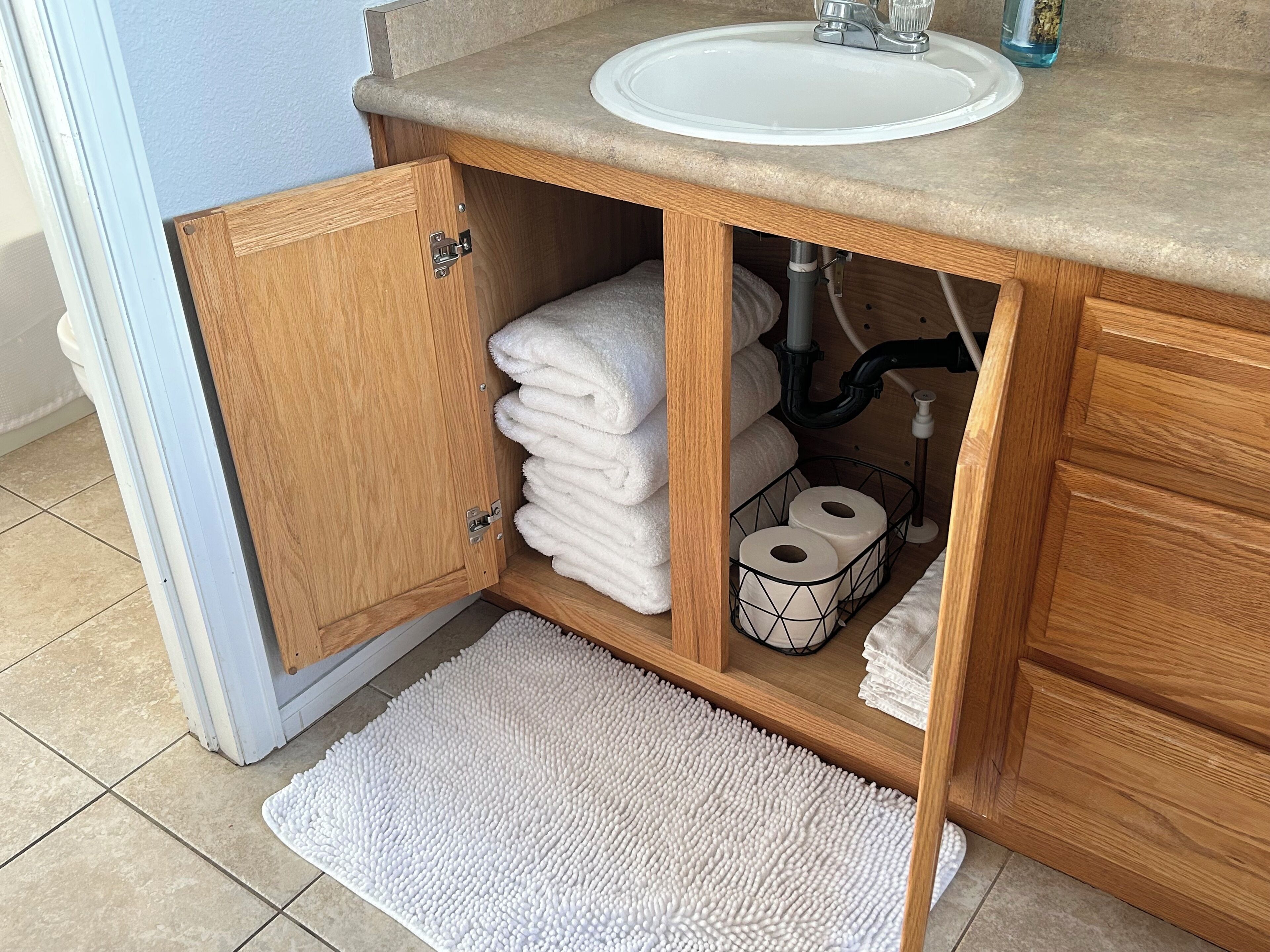 A wooden bathroom vanity with a white sink, a towel rack, and a toilet paper holder.