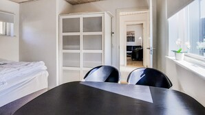 Ein Hotelzimmer mit einem Bett, einem Esstisch, zwei Stühlen, einem Kleiderschrank und einem Fenster mit einer Pflanze.