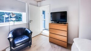Ein Zimmer mit einem schwarzen Ledersessel, einer Holzkommode mit Fernseher darauf und einem Fenster mit Blick ins Grüne.