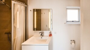 Ein Badezimmer mit einem weißen Waschbecken, einem Spiegel, einer Dusche und einem Fenster.