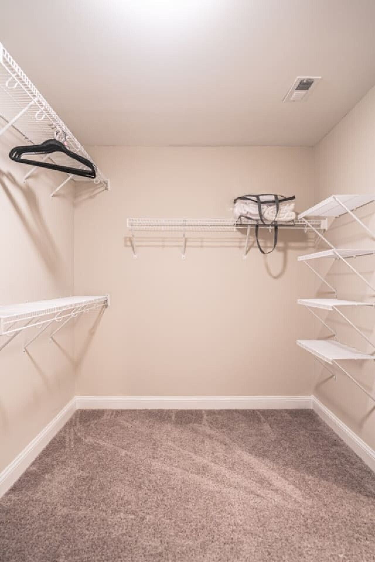 A small, empty walk-in closet with white shelving units and a beige carpet.