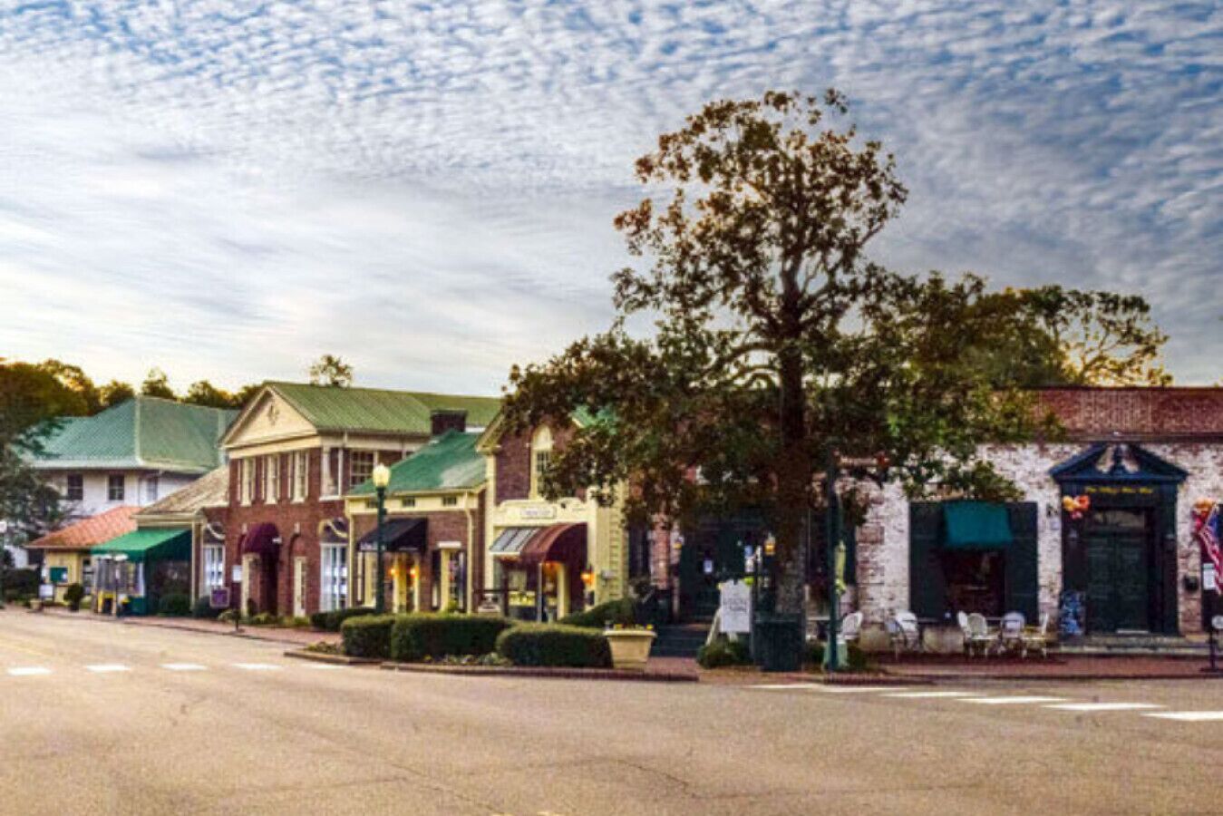 A street view with historic buildings, a tree-lined sidewalk, and a clear sky.