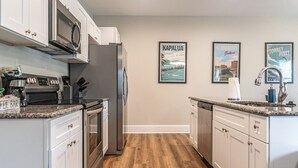A modern kitchen with white cabinets, stainless steel appliances, and wooden flooring. There are framed pictures on the wall and a coffee bar on the counter. - Ducks Landing Accommodations at Southern Pines Golf Course (Aberdeen)
