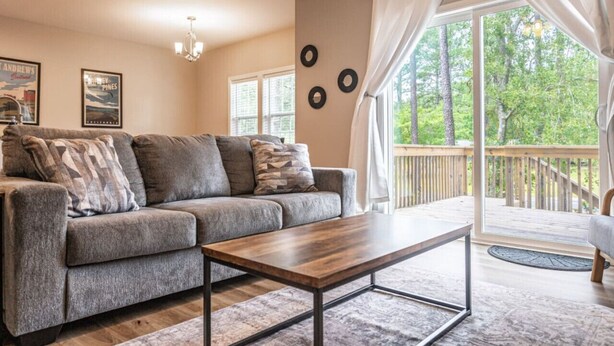 A living room with a gray sofa, a wooden coffee table, and a view of a deck through large windows. - Ducks Landing Accommodations at Southern Pines Golf Course (Aberdeen)