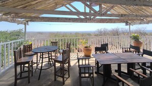 An outdoor patio with wooden tables and chairs, a thatched roof, and a view of the landscape. - Room in Lodge - Zambezi Boutique Lodge Suite 1 With Free 4x4 Tour by Savannah Adventures (Victoria Falls)