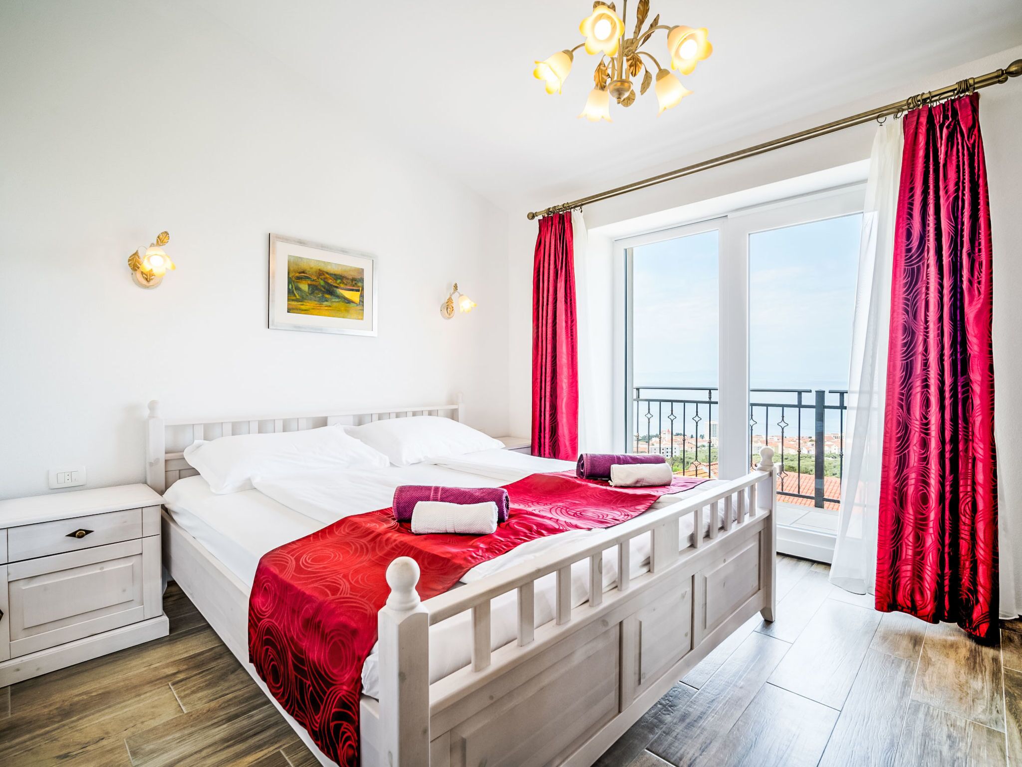 Una camera da letto con un letto, un comodino, un quadro e un balcone con tende rosse.