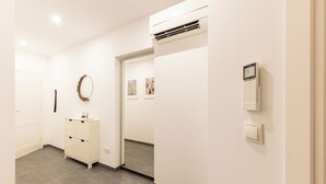 Een gang met een witte muur, een deur, een wit kastje en een airconditioning.