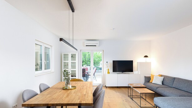 Una sala de estar moderna con una mesa de comedor de madera, un sofá gris y un televisor de pantalla plana.
