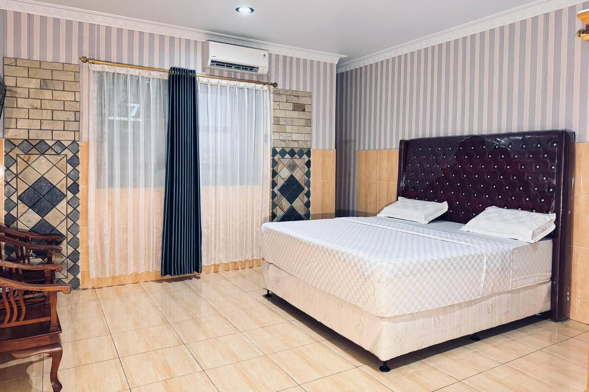 A hotel room with a bed, curtains, an air conditioning unit, and a tiled floor.