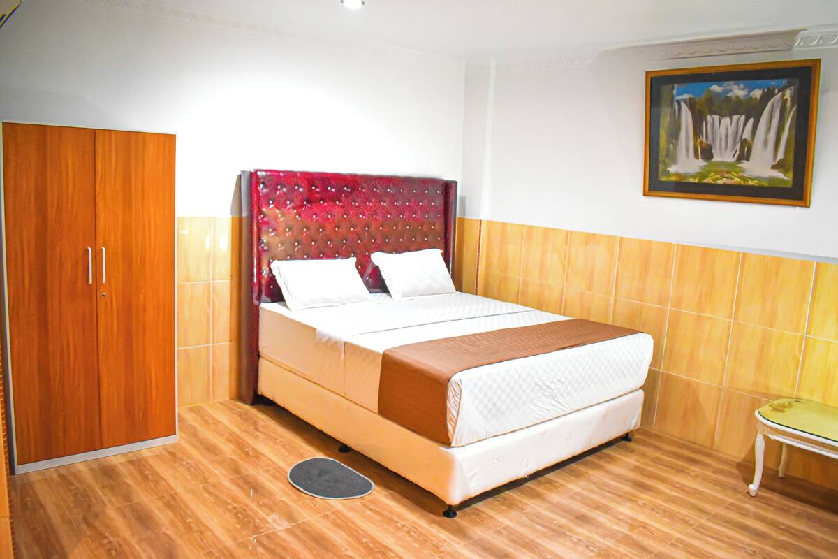 A bedroom with a bed, a wardrobe, a painting, and a small table.