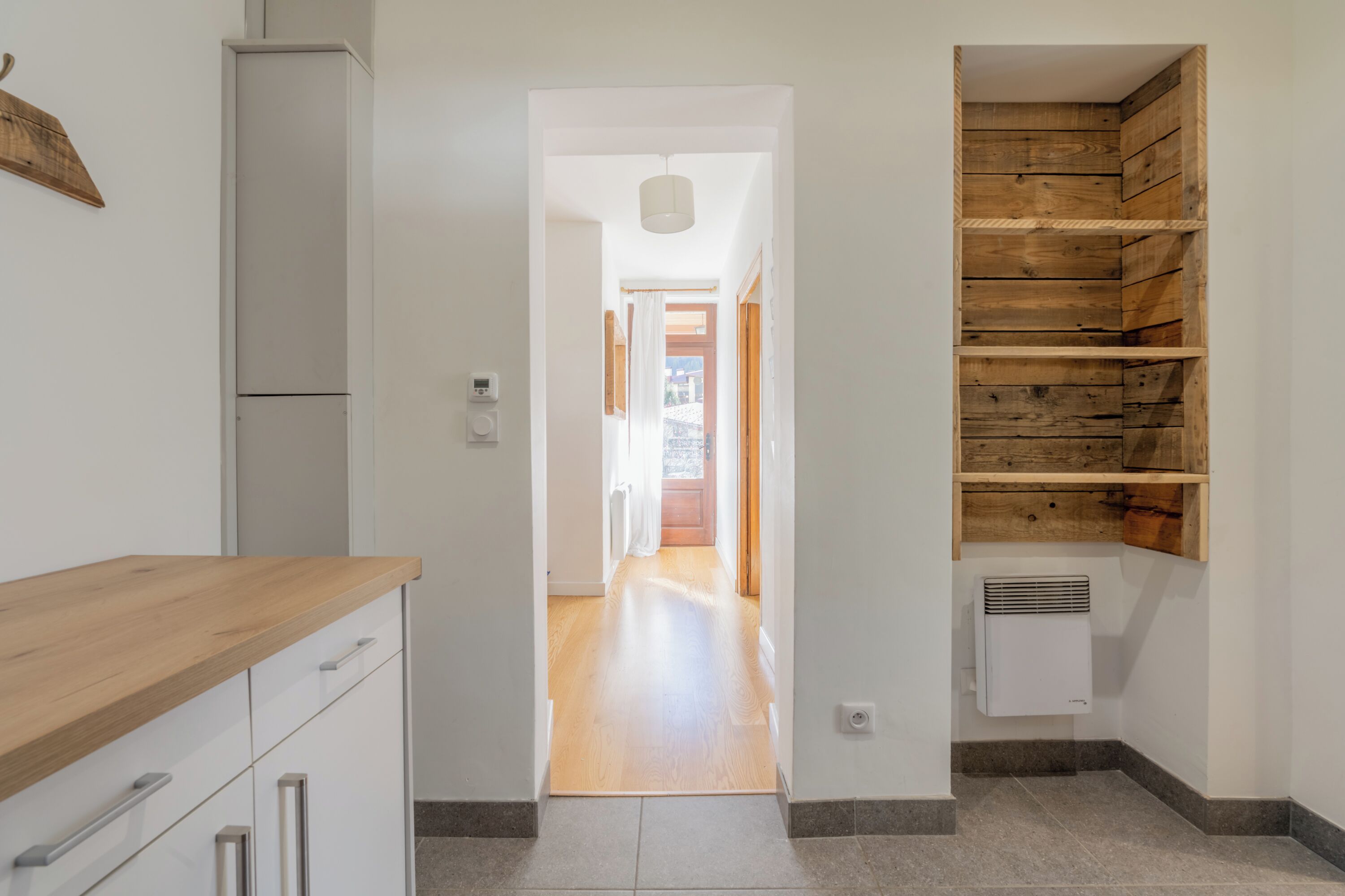 A narrow hallway with a wooden counter on the left and a built-in wooden shelf unit on the right.