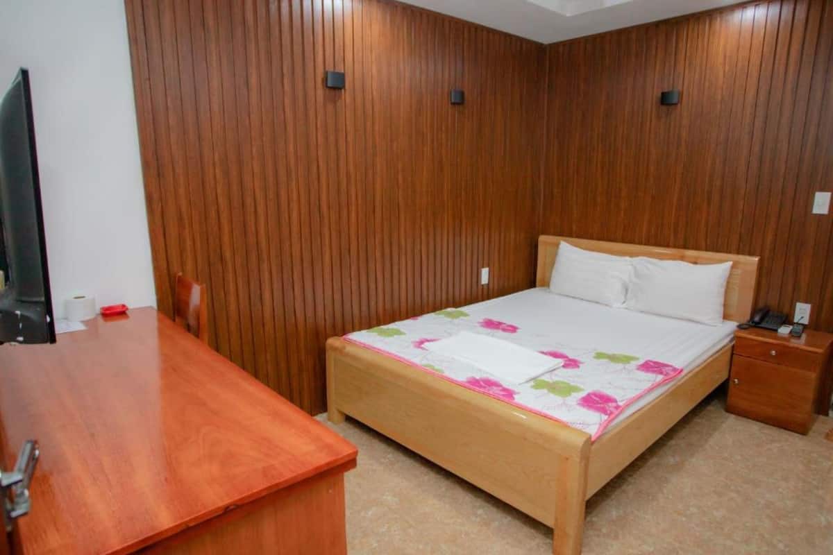 Un dormitorio con una cama de madera, una mesita de noche de madera, un escritorio de madera y un televisor.