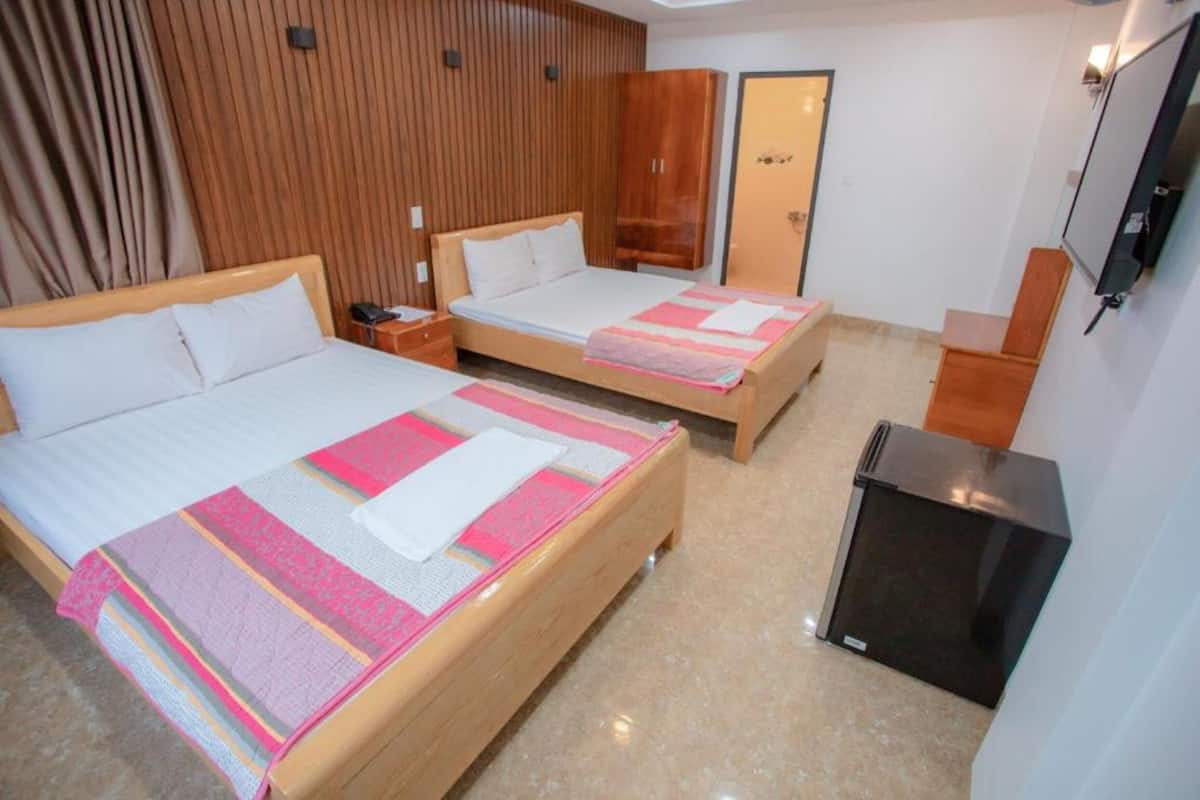 Habitación de hotel con dos camas, armario de madera, un escritorio pequeño y un televisor.