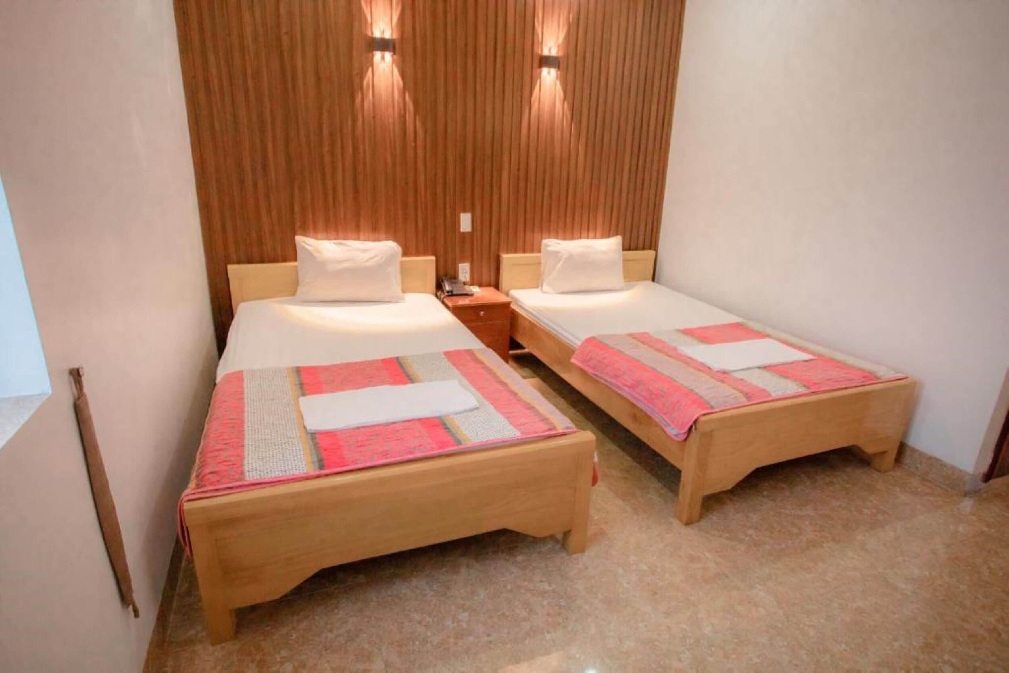 Une chambre avec deux lits simples, chacun doté d’une tête de lit en bois et d’une table de chevet.