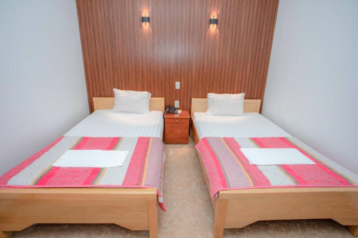 Habitación doble con dos camas individuales, cabeceros de madera, una mesita de noche y un panel de pared de madera.