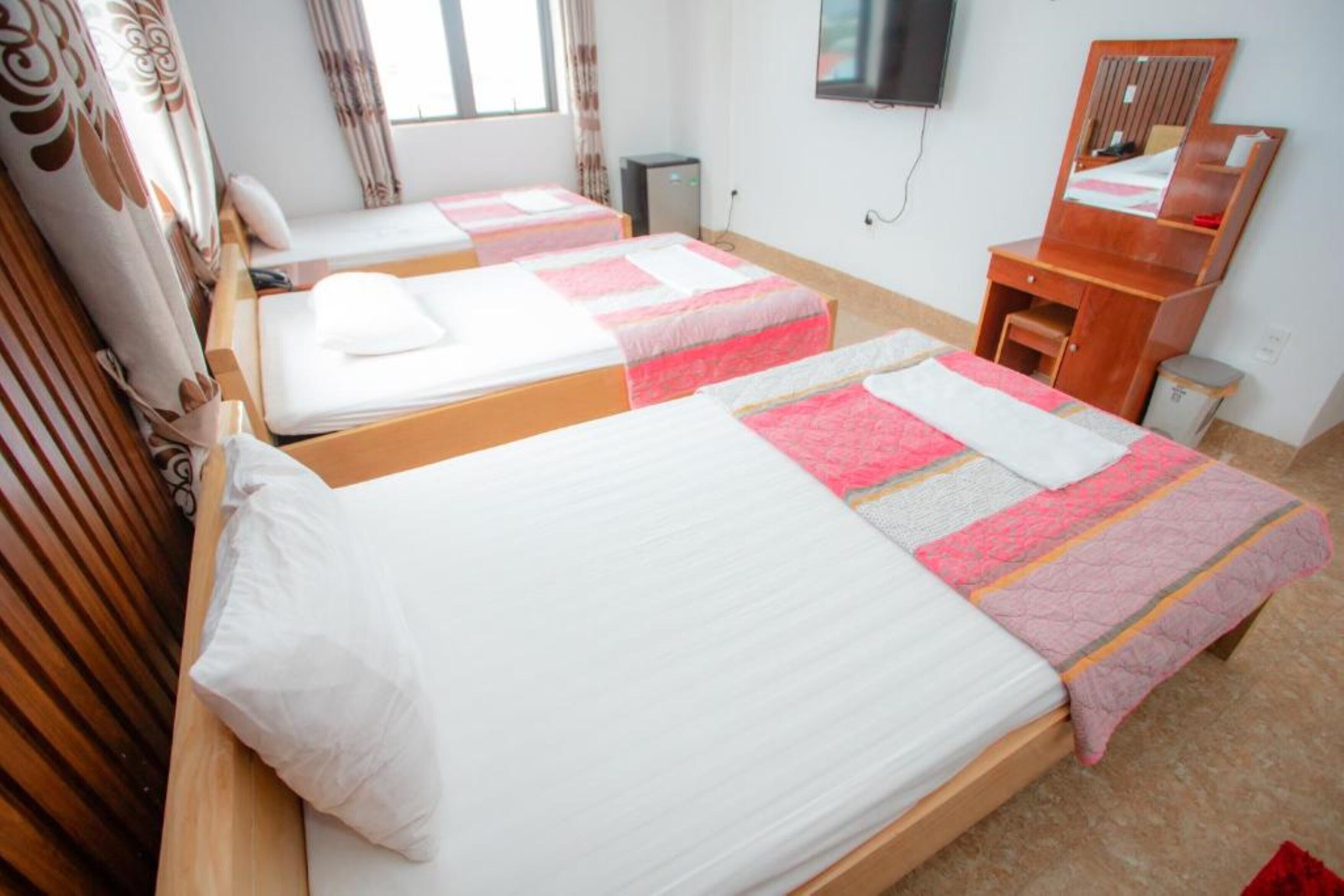 A hotel room with two single beds, a wooden dresser, a television, and a window with curtains.