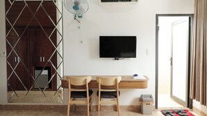 Une chambre d’hôtel équipée d’un bureau, de deux chaises, d’une télévision, d’un ventilateur et d’une porte.