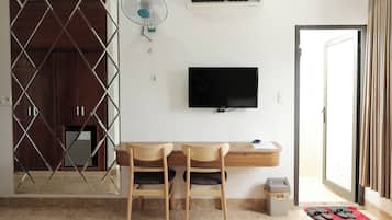 A hotel room with a desk, two chairs, a TV, a fan, and a door.