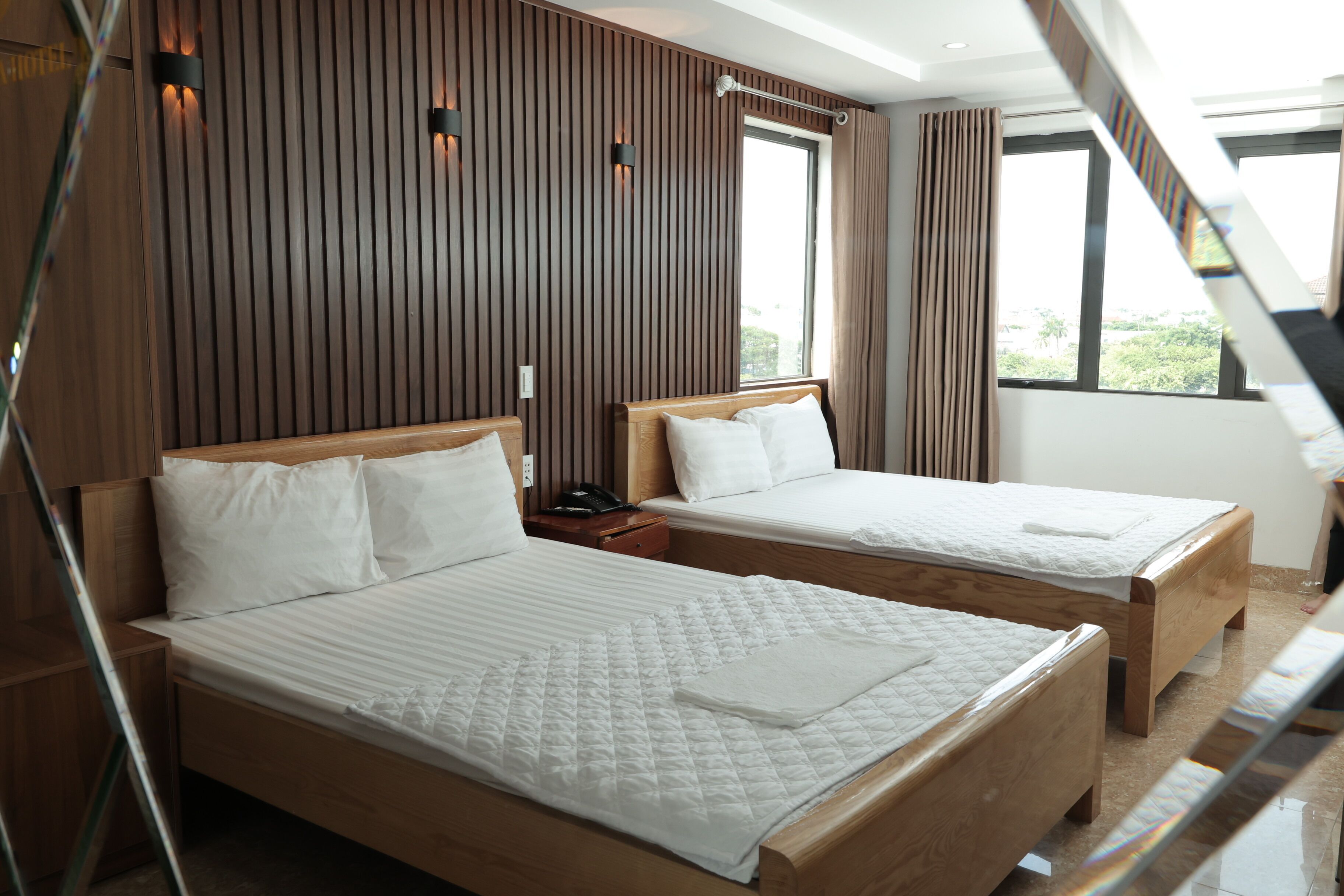 Ein Hotelzimmer mit zwei Holzbetten, einem Nachttisch und einem Fenster mit Vorhängen.