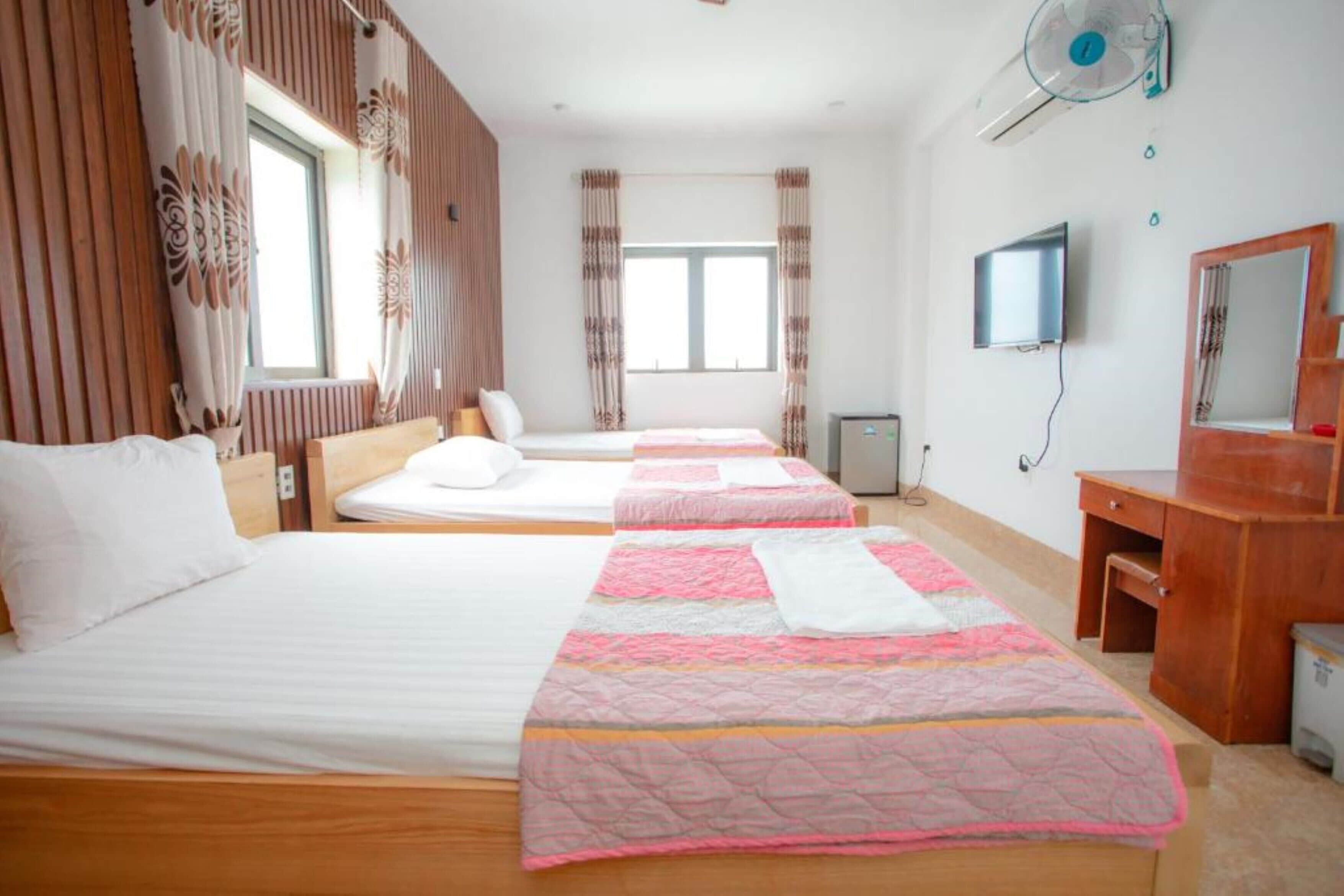 Una habitación de hotel con tres camas, un escritorio de madera, un televisor y un espejo.
