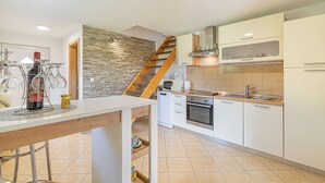 Een moderne keuken met een accentmuur van steen, een houten trap en witte kastjes.