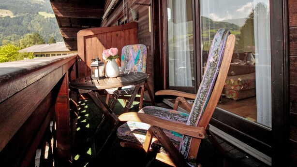 Ein Holzbalkon mit Tisch und Stühlen, einer Blumenvase und Blick auf die Berge.
