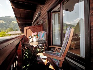 Un balcon en bois avec une table et des chaises, un vase rempli de fleurs et une vue sur les montagnes.