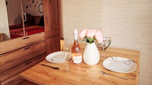 Ein Holztisch mit einer Flasche Brillat-Sagutti Wein, einer Vase mit rosa Blumen und einem Weinglas.