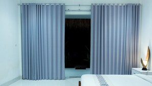 A hotel room with a bed, curtains, a bedside table, and a lamp. - Turtle House Lombok (Kuta)