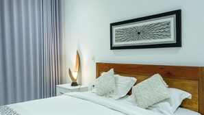 A neatly made bed with white bedding and decorative pillows, a bedside lamp, and a framed abstract artwork on the wall. - Turtle House Lombok (Kuta)