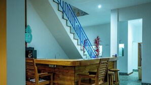 A kitchen with a wooden bar counter, chairs, a blue staircase, and a tiled floor. - Turtle House Lombok (Kuta)