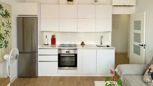 A modern kitchen with white cabinets, a stainless steel refrigerator, an oven, and a microwave. There is a dining area with a white table and chairs, and a living room with a sofa and a coffee table. - DELUX Penthouse International Center (Llanos, Los (Torrox-Costa))