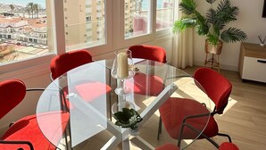 A modern living room with a glass table and red chairs, large windows with a view of the sea and buildings, and a potted plant. - DELUX Penthouse International Center (Llanos, Los (Torrox-Costa))
