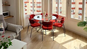 A modern living room with a round glass table, red chairs, a white sofa, and large windows with a view of buildings. - DELUX Penthouse International Center (Llanos, Los (Torrox-Costa))
