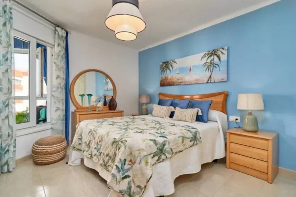 A bedroom with a bed, a nightstand, a lamp, a mirror, and a painting on the wall.