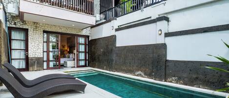 Una piscina con una tumbona, un muro de piedra y un balcón con barandilla.