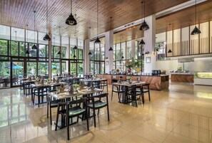 Een ruime restaurantruimte met hoge plafonds en grote ramen, houten vloeren en moderne hanglampen.