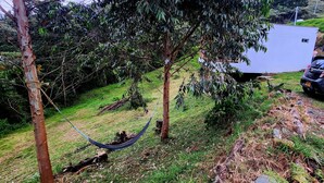 A grassy area with a hammock, trees, a white building, and a parked car. - Cabaña en la Montaña con Vista a la Ciudad Desde el Jacuzzi (Medellín)