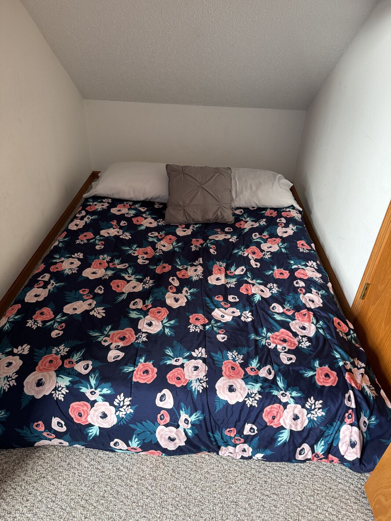 A small, single-bed room with a dark floral bedspread and two pillows.