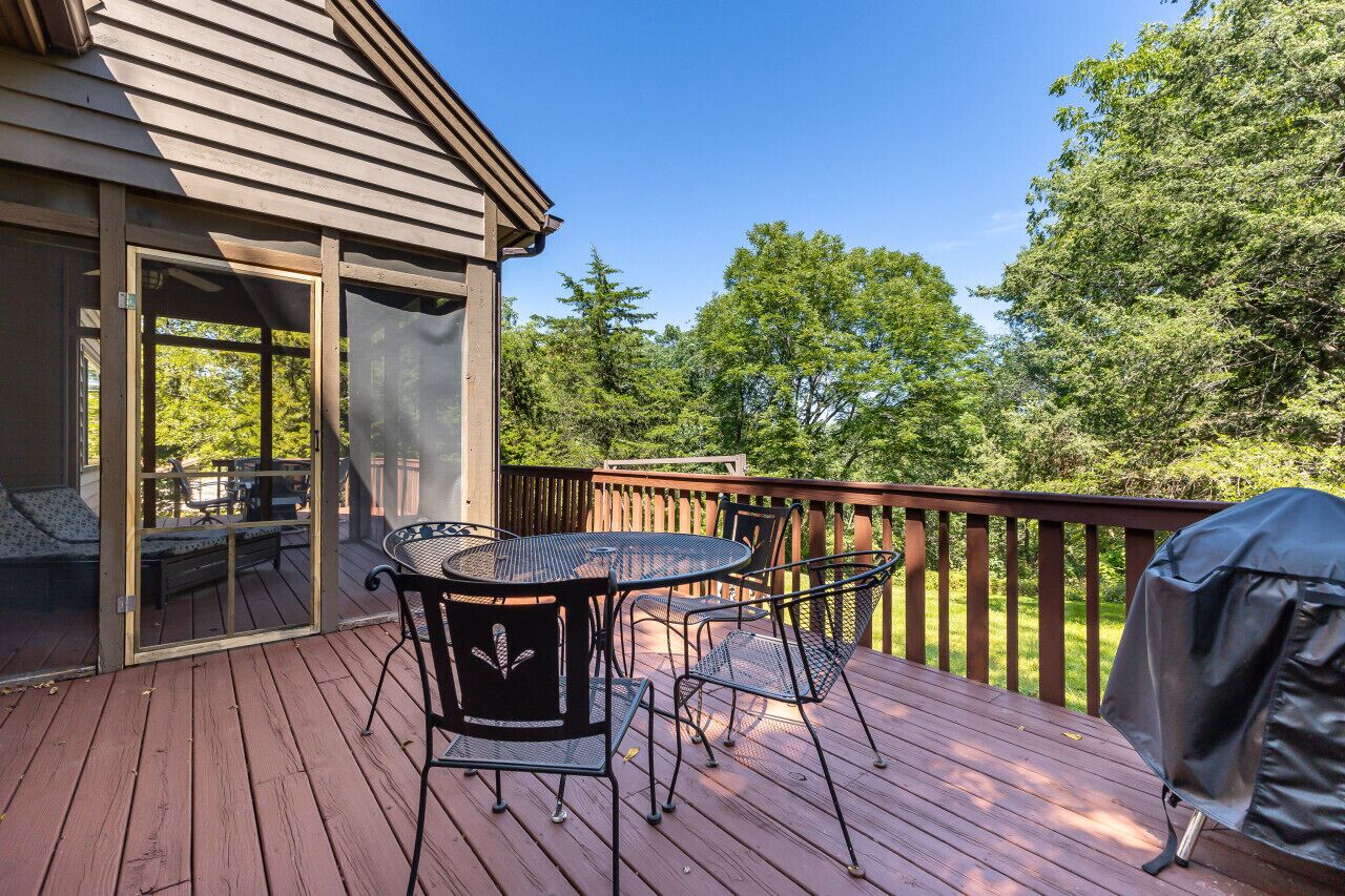 Eine Holzterrasse mit Tisch und Stühlen, einem Grill und einem überdachten Patio.