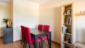 A dining area with a dark wooden table and red upholstered chairs. There is a bookshelf to the right with books and decorative items. - GuestReady - Hideaway in Porto (Porto)