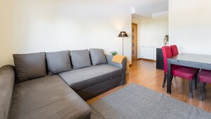 A modern living room with a grey sofa, a dining table with red chairs, a floor lamp, and a radiator. - GuestReady - Hideaway in Porto (Porto)
