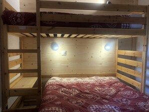 A bunk bed with a patterned bedspread, wooden walls, and two wall-mounted lights. - Le Cheval Noir 20 - 2 Pièces Joliment Rénové Avec Grande Terrasse (LES AVANCHERS VALMOREL)