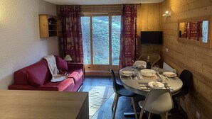 Tunnelmallinen huone, jossa on punainen sohva, neljälle katettu ruokapöytä ja seinälle asennettu televisio.
