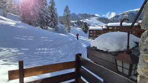 A snow-covered ski slope with a wooden bench and a building in the background. - Le Cheval Noir 20 - 2 Pièces Joliment Rénové Avec Grande Terrasse (LES AVANCHERS VALMOREL)