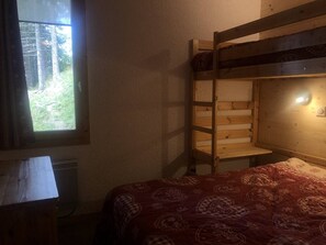 Ein Stockbett mit Holzrahmen, ein Fenster mit Vorhängen und eine gestreifte Bettdecke.