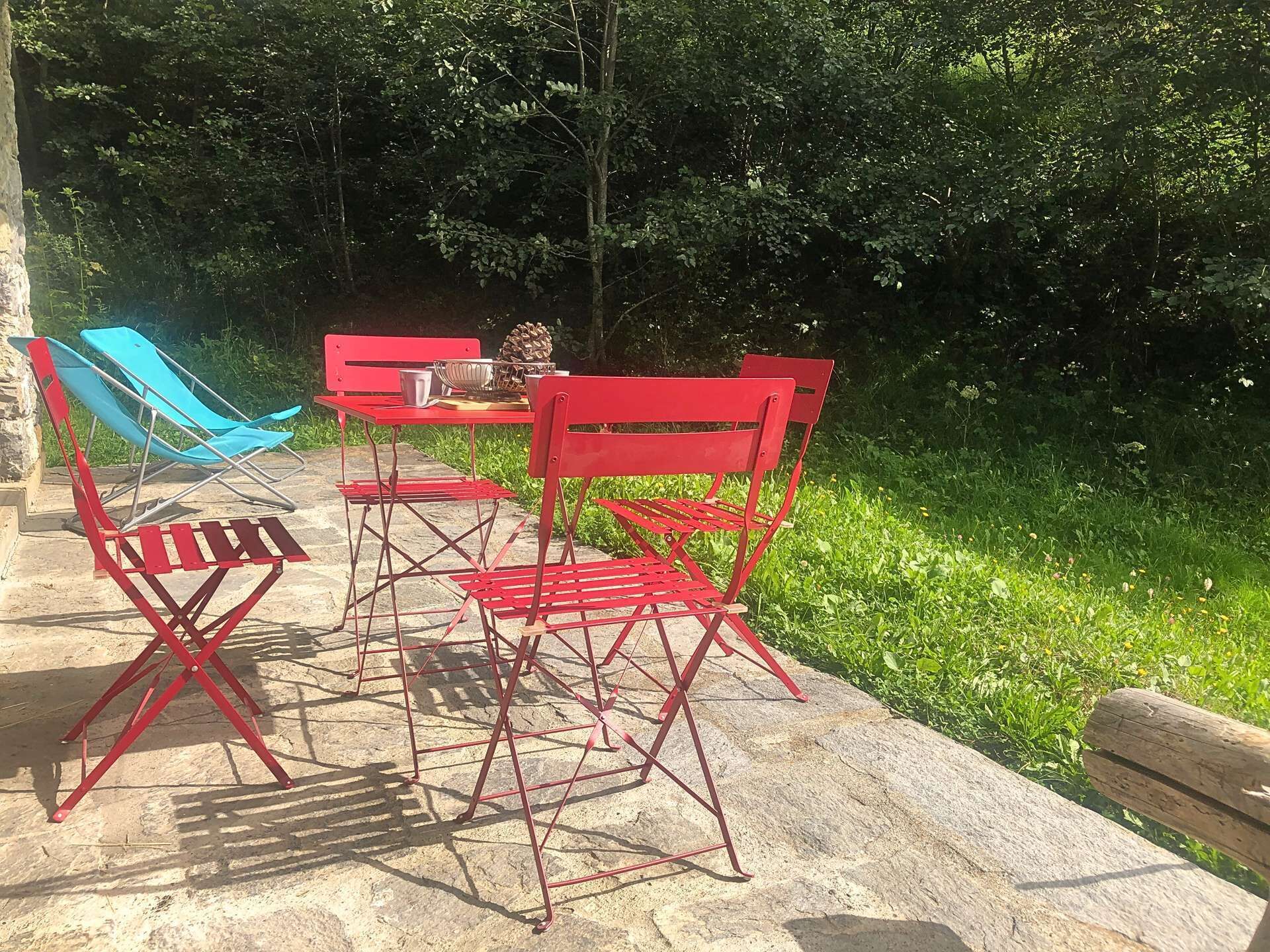 A red metal table and chairs set outdoors with a natural backdrop.