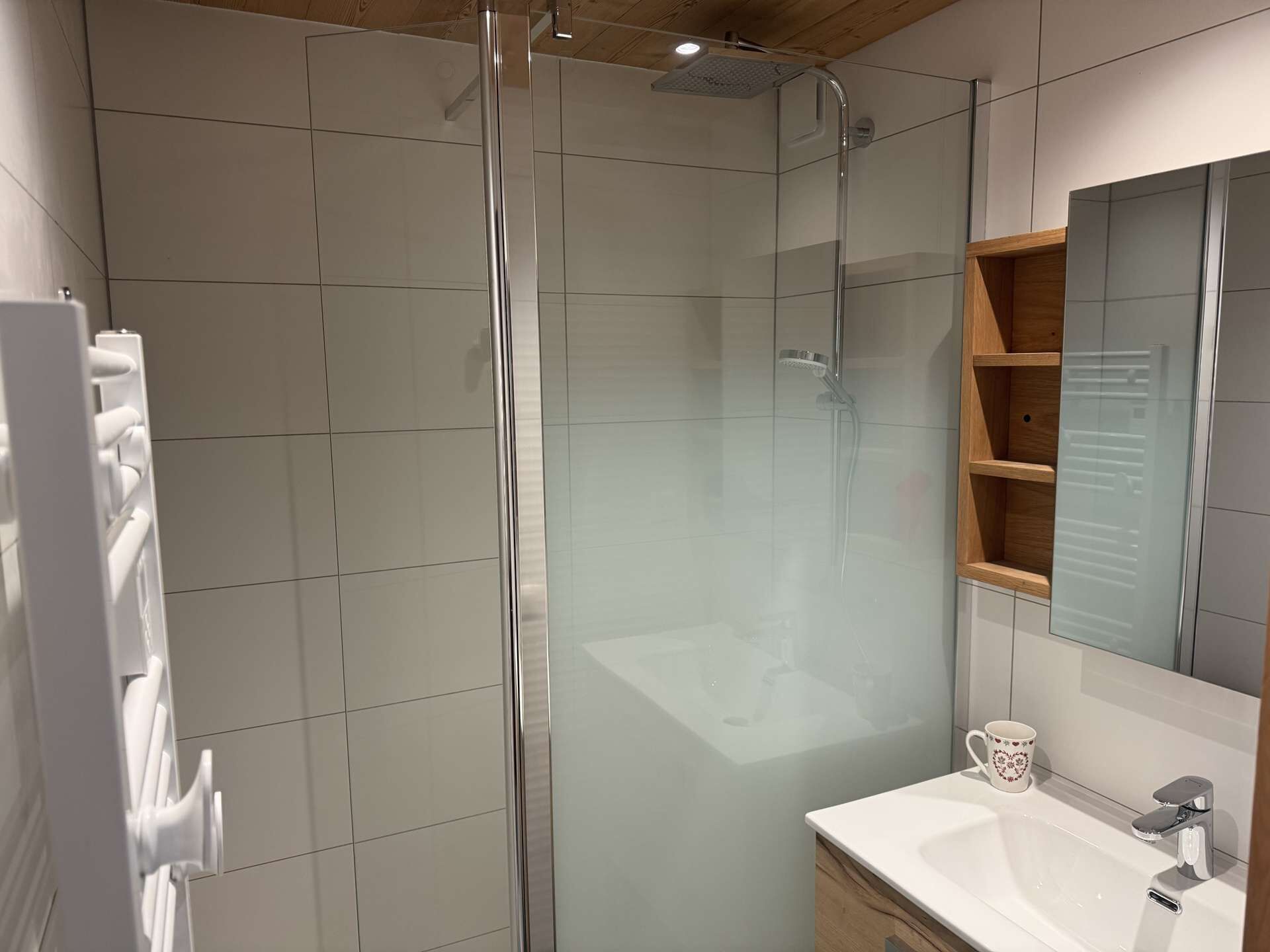 Ein modernes Badezimmer mit einer Duschkabine, einem weißen Waschbecken und einem Holzbadezimmer-Möbel.